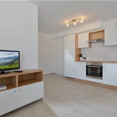 Eine moderne Küche mit weißen Schränken und einem Fernseher. Der Raum ist hell und einladend.