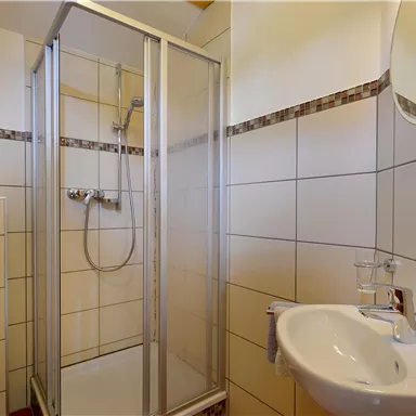A modern bathroom with a shower stall, a sink, and a mirror. The walls are brightly tiled and the furnishings are clean and functional.