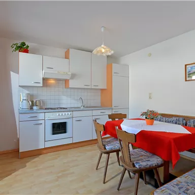 A modern kitchen with a dining area and red tablecloths. Bright walls and windows create a friendly atmosphere.