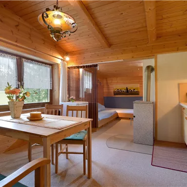 A cozy vacation apartment with wooden ceilings and colorful furniture. The space includes a seating area, a dining area, and a small kitchen.