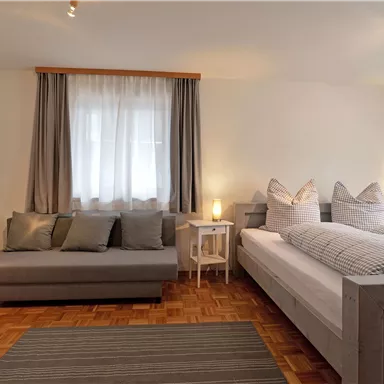 A bright and modern bedroom with a double bed and a cozy sofa. The large windows provide plenty of daylight and an inviting atmosphere.