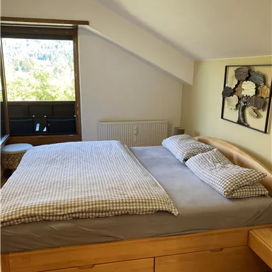 Ein gemütliches Schlafzimmer mit einem großen Bett und Kissen. Der Raum hat ein Fenster mit Blick ins Freie und Holzfußboden.