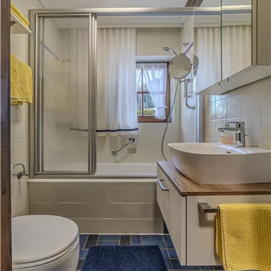 Ein modernes Badezimmer mit einer Dusche und Badewanne. Die weißen Wände und gelben Handtücher schaffen eine helle, frische Atmosphäre.