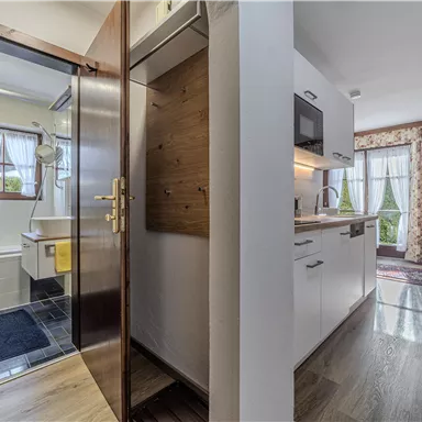 Ein modernes Badezimmer mit Dusche und hellen Vorhängen ist sichtbar. Daneben eine moderne Küche mit Holzregalen und Fenster mit Aussicht.