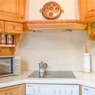 A cozy kitchen with wooden furniture and modern appliances. On the countertop sits an espresso maker and there is a microwave.