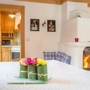 A cozy living space with a comfortable fireplace and a wood-paneled kitchen. On the table, colorful flowers are arranged in a decorative display.