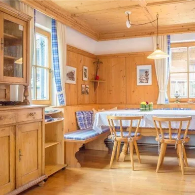 A cozy dining area made of wood with a large table and chairs. The walls are bright and equipped with windows that let in a lot of light.