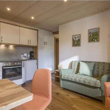 Eine moderne Küche mit einem Essbereich und einem gemütlichen Sofa. Der Raum hat warmes Holz und helle Farben, die eine einladende Atmosphäre schaffen.