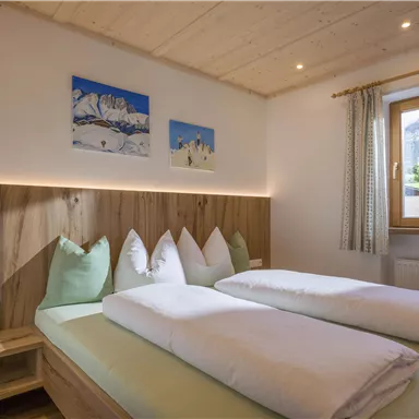 Ein gemütliches Schlafzimmer mit zwei Betten und holzverkleideten Wänden. Durch das Fenster sieht man eine schöne Aussicht auf die Berge.