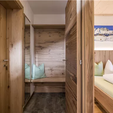 Ein modernes Zimmer mit Holzverkleidung und einem gemütlichen Bett. Auf der linken Seite befindet sich ein Spiegel und eine Sitzgelegenheit.