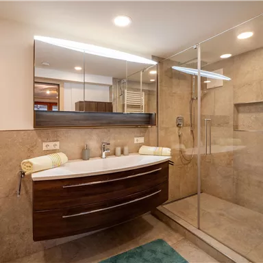 A modern bathroom with a large shower and an elegant vanity. The walls are decorated with beige tiles and there is a soft, blue carpet.
