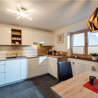 A modern kitchen with white cabinets and wooden details. A table with chairs and decorative elements invites you to dine.