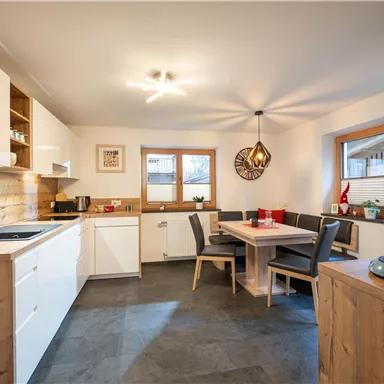 A modern kitchen with wood and white tones. There is a dining area with a table and chairs, as well as ample daylight.