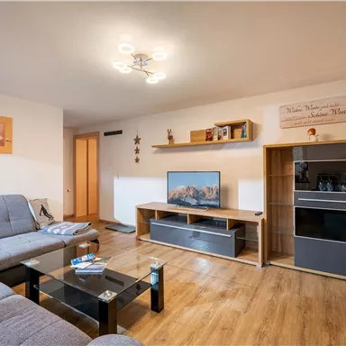 A cozy living room with a modern couch and a TV. The space is bright and offers an inviting atmosphere.