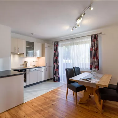 A modern kitchen with bright cabinets and a dining table. The large windows let in plenty of daylight.