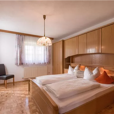 A cozy bedroom with a double bed and wooden furniture. The large windows provide plenty of daylight.