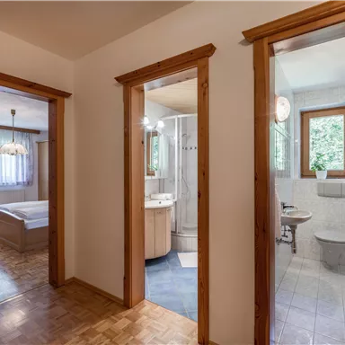 A corridor with two open doors to the bathroom and bedroom. The room has bright walls and wood paneling.