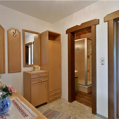 An entrance area with wooden furniture and mirrors. On the table, there is a vase with flowers, and the room has a cozy atmosphere.