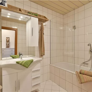 A modern bathroom with bright tiles and a bathtub. Green towels and accessories add a fresh touch.