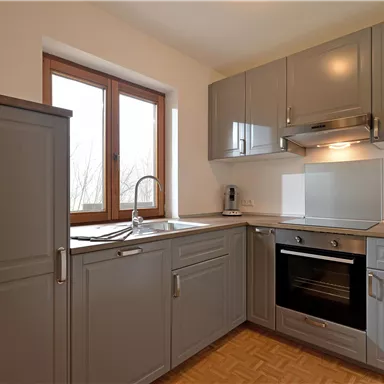 A modern kitchen with gray cabinets and elegant appliances. The light from the windows creates a bright and inviting atmosphere.