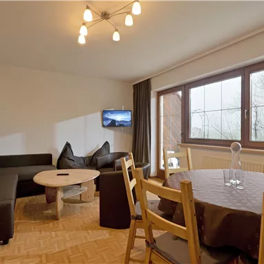 A modern living room with a cozy sofa and a round table. Large windows provide a view of the outside and let in plenty of daylight.