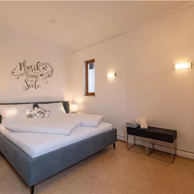 A modern bedroom with a large bed and stylish furniture. The walls are light, and a decorative font gives the space character.