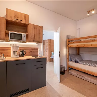 A modern kitchen with wooden cabinets and a microwave. The room features a bunk bed and a cozy atmosphere.