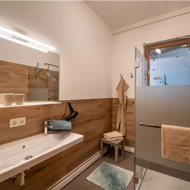 A modern bathroom with wooden paneling and a shower. There is a sink, towels, and pleasant lighting.