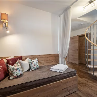 A cozy room with a wooden bench and colorful cushions. A curved staircase leads to the next floor.