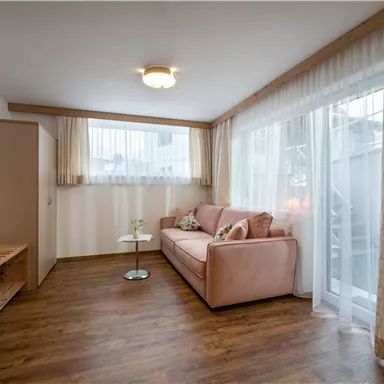 A cozy living room with a pink sofa and a small table. Large windows provide plenty of natural light and a friendly atmosphere.