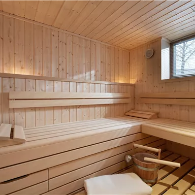 A cozy sauna made of light wood with ample space to relax. Daylight streams in through the window.