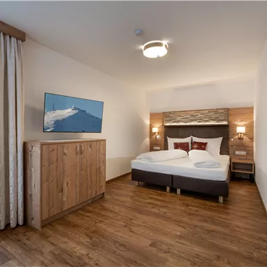 A modern room with a double bed and wooden flooring. A television is mounted on the wall, and there are curtains that create a warmer ambiance.