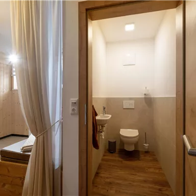 A modern bathroom with a toilet and bright light. The walls are in neutral colors and the floor is made of wood.
