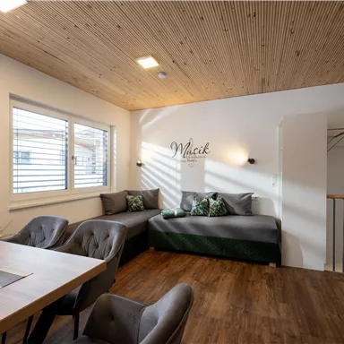 A modern living room with a cozy sofa and a table. The walls are bright and the wooden ceiling creates a warm atmosphere.