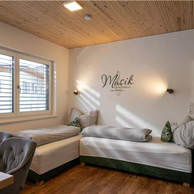 A cozy room with two single beds and a wooden floor. The walls are light, and a window lets in plenty of daylight.