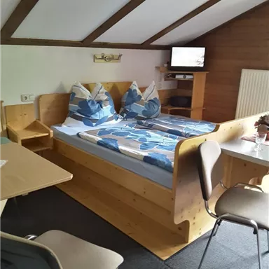 A cozy bedroom with a double bed, atmospheric decor, and a TV. There is also a table and chairs for sitting.