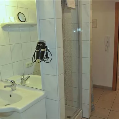A simple bathroom with a sink, a mirror, and a shower. In the background, a separate toilet is visible.
