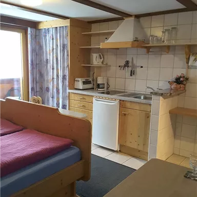 A cozy vacation apartment with a bed, a small kitchenette, and a table. Large windows let in plenty of light and offer a view outside.
