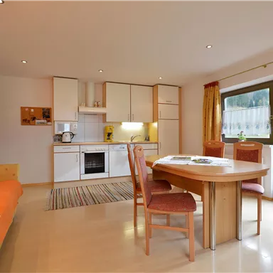 A modern living room with a dining table and chairs. The large window front offers a beautiful view of the garden.