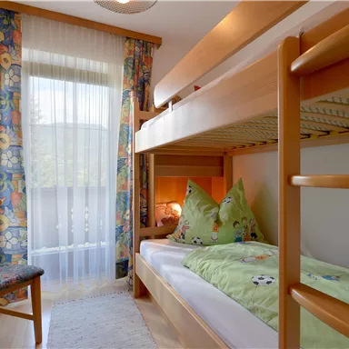 A cozy children's room with a bunk bed and colorful curtains. A chair is next to the window, which lets in a lot of light.
