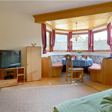 A cozy living space with a seating area and large windows. The room is furnished with wooden furniture and a television.