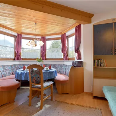 A cozy dining area with a round table and upholstered benches. Large windows with curtains let in plenty of light and create an inviting atmosphere.