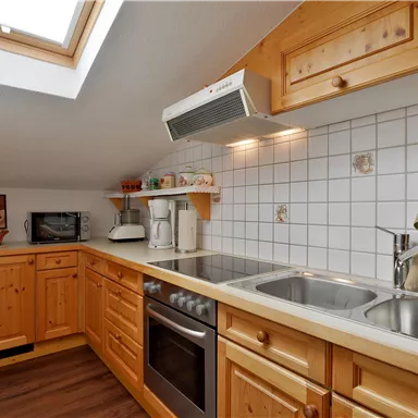 A modern kitchen with wooden cabinets and white tiles. The skylight provides plenty of daylight.