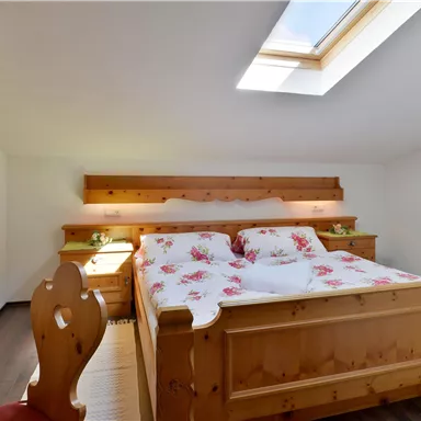 A cozy bedroom with a large wooden bed and bright linens. The room has a skylight that lets in plenty of natural light.