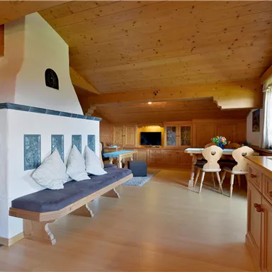 A cozy living space with wooden walls and a modern fireplace.  
The room features a bench, a dining table, and large windows that let in plenty of light.