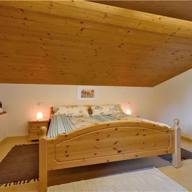 A cozy bedroom with a wooden bed and sloping ceilings. Next to the bed are nightstands with soft lamps.