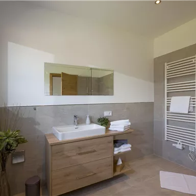 A modern bathroom with a large shower and a wooden wash area. The walls are in neutral colors and there are plants for a pleasant atmosphere.