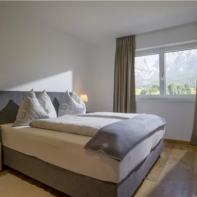 A cozy room with a double bed and beautiful pillows. A picturesque mountain landscape can be seen through the window.