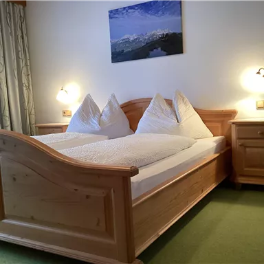 A cozy bedroom with a wooden double bed and two pillows. A picture of a mountain landscape hangs on the wall.