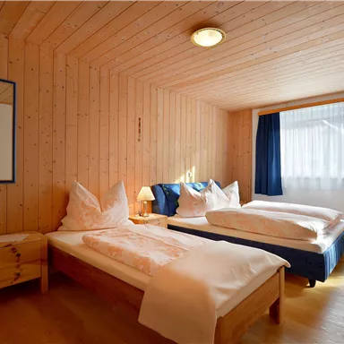 Ein gemütliches Zimmer mit zwei Einzelbetten und holzverkleideten Wänden. Das Fenster lässt natürliches Licht herein und bietet einen Blick nach draußen.